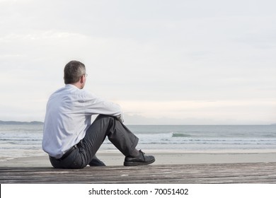 Thoughtful businessman sitting on a beach and looking at the sea - Powered by Shutterstock