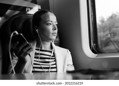Thoughtful Businesswoman Listening To Podcast On Mobile Phone While Traveling By Train.