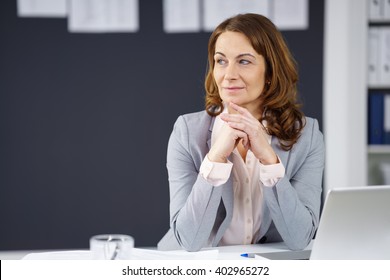 Thoughtful businesswoman sitting at her desk in the office looking to the side watching something, with copy space