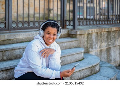 Thoughtful calm and peaceful young woman seat on steps and listening to music alone on steps.  Wireless earphones in ears. Moder smartphone in hand. - Powered by Shutterstock