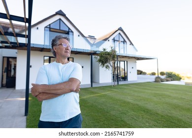 Thoughtful caucasian senior man with arms crossed standing against nursing home in yard, copy space. Contemplation, unaltered, support, assisted living and retirement home. - Powered by Shutterstock