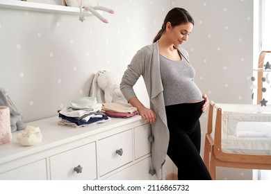 Thoughtful caucasian woman in advanced pregnancy standing in the baby's room next to the crib - Powered by Shutterstock