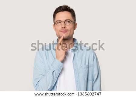 Thoughtful Caucasian young male in glasses touch chin with finger thinking or considering, pensive European man wearing spectacles isolated on grey studio background making decision or imagining