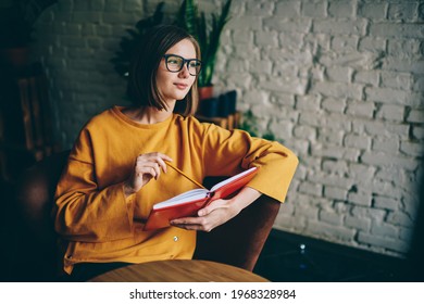Thoughtful clever student in optical eyeglasses for vision protection pondering on interesting best seller plot, contemplative young woman with short haircut holding education textbook and learning - Shutterstock ID 1968328984