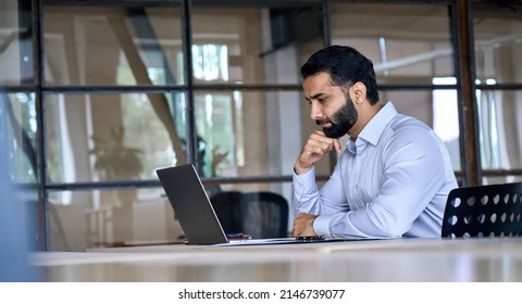 Thoughtful concentrated indian business man entrepreneur investor manager using computer  watching webinar working in office analyzing online data market thinking doing web research looking at laptop 