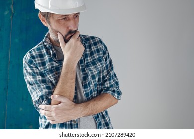 Thoughtful construction foreman in holding chin pose. Adult caucasian male with white hard hat.