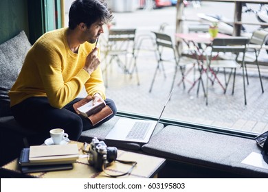 Thoughtful Creative Writer Looking Out Window Of Coffee Shop Sitting Inside In Front Of Laptop Computer Working On Book Noting Ideas Into Notepad Waiting For Inspiration Imagine Plot Of Story  