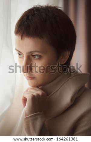 Thoughtful dark-haired woman standing at the window