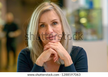 Thoughtful determined middle-aged woman scrutinising the camera with her chin resting on her hands