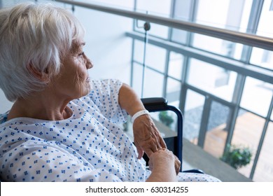 Thoughtful disabled senior patient on wheelchair in hospital passageway at hospital - Powered by Shutterstock