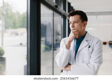 A thoughtful doctor in a white coat stands by the window in a modern clinic. - Powered by Shutterstock