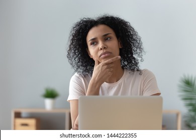 Thoughtful doubtful african female student worker looking away thinking solving problem feel lack of new creative ideas at work, pensive puzzled or bored young black woman sit at desk with laptop