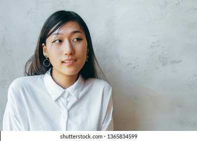 Thoughtful Doubtful Beautiful Asian Girl In White Shirt With Unsure Face Holding Hand On Chin Looking At Copy Space, Teen Girl Feeling Hesitant Uncertain Thinking On Grey Studio Background.