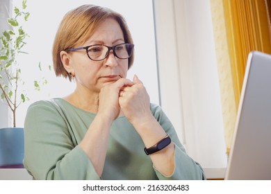 Thoughtful Elderly Blonde Woman In Eyeglasses Looking On Laptop Screen From Home Ponder On Document. Pensive Retiree Female Freelancer Remote Student Learn Online Thinking On Video Lecture Material