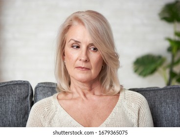 Thoughtful Elderly Lady. Sad Old Woman Is Sitting On A Sofa At Living Room