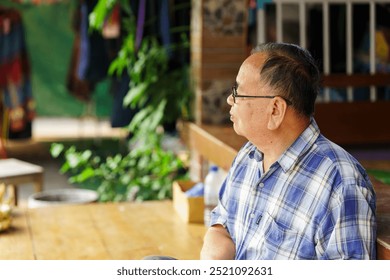 A thoughtful elderly man enjoying a moment of reflection, seated in a tranquil environment surrounded by greenery and warm light, conveying a sense of peace and contemplation. - Powered by Shutterstock