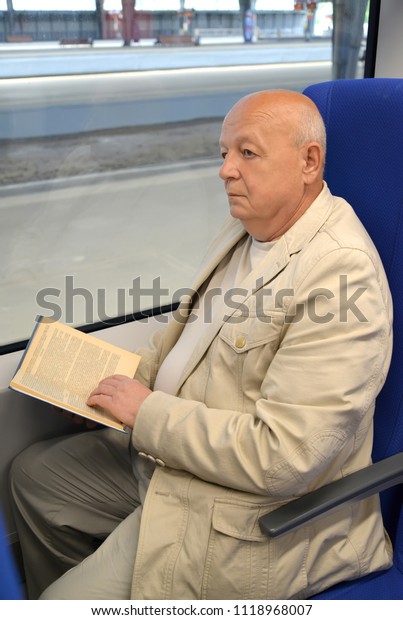 The thoughtful elderly man reads the book in the\
electric train car