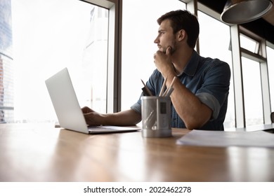 Thoughtful Employee, Business Man, Manager Looking Out Of Window In Deep Thought, Sitting At Workplace With Laptop In Office, Thinking Over Company Future, Pondering On Decision For Work Task