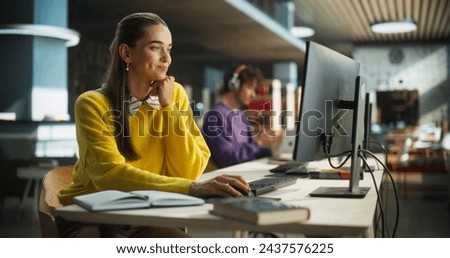 Thoughtful European College Student Using Desktop Computer to Study in a Public Library. Beautiful Young Woman Learning Online, Getting Ready for Exams, Taking Notes and Drafting an Essay