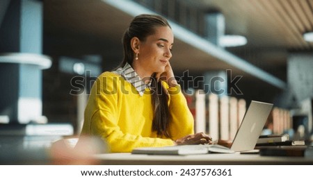 Thoughtful European College Student Using Laptop Computer to Study in a Public Library. Beautiful Young Woman Learning Online, Getting Ready for Exams, Taking Notes and Drafting an Essay