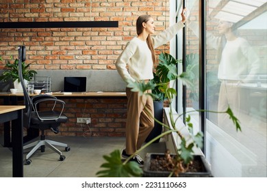 Thoughtful  female entrepreneur looking through window in small startup office - Powered by Shutterstock