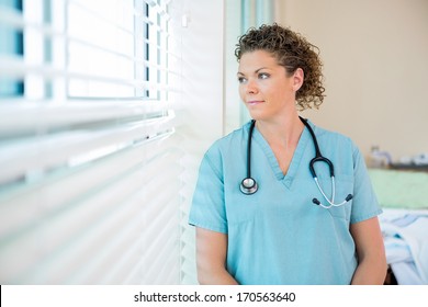 Thoughtful Female Nurse Looking Out Through Window In Hospital Room