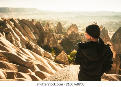 Thoughtful Female Person Stand Look Over Dramatic Valley On Hazy Morning Sunrise With Fairy Chimneys Background. Solo Exploration In Turkey. Cinematic Travel Destination-Cappadocia