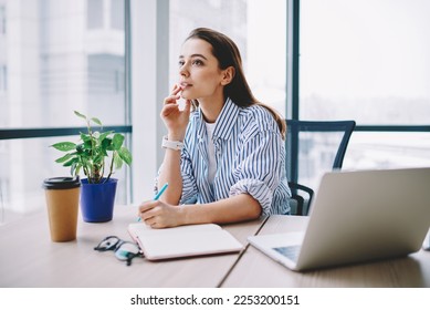 Thoughtful female rewriter in smart casual clothing sitting at table desktop with laptop computer and working with ideas for SEO text,pensive content manager planning project organisation in workspace