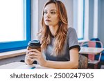 Thoughtful female student pondering on essay for university during coffee break indoors, young pensive woman holding takeaway cup sitting at desktop with notebook and thinking about education