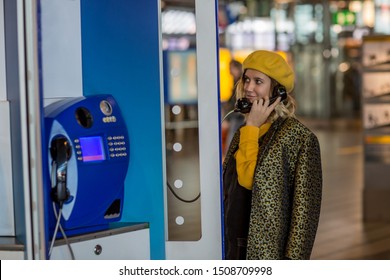 Thoughtful Female Tourist Making Call In Payphone On Street Standing In Transparent Booth, Young Woman Using Public Telephone Operated With Coins During Travel For Call With Low Prices Abroad