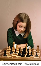 Thoughtful Focused Young Female Chess Player Reflects On Position Pieces In Chess Game. School Child Girl Sitting At Chessboard In Green Dress. Middlegame. Move White Pieces