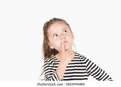 Achtsames Mädchen schaut zur Seite und berührt ihren Mund mit dem Finger. Mädchen mit seitlich gerichteten Augen und Kopf geneigt zu einer Seite. Posing kleine Mädchen mit gestreiftem Hemd. Einziger Hintergrund.