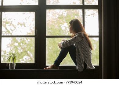Thoughtful girl sitting on sill embracing knees looking at window, sad depressed teenager spending time alone at home, young upset pensive woman feeling lonely or frustrated thinking about problems - Shutterstock ID 793940824