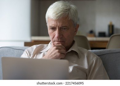 Thoughtful Grey-haired Mature Man Learning Laptop App Or Software, Looking Pensive And Serious Sit On Sofa At Home, Close-up. Older People Using Modern Tech, Experiences Difficulties With Technology