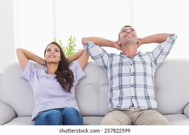 Thoughtful Happy Couple With Hands Behind Head Sitting On Sofa At Home