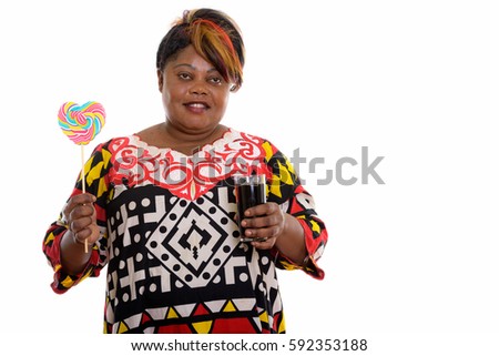 Thoughtful happy fat black African woman smiling while holding heart shaped lollipop and glass of soda drink