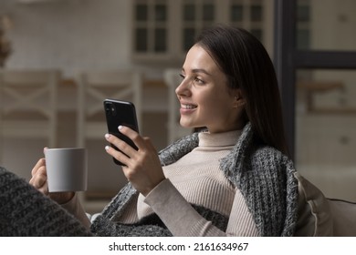 Thoughtful Happy Mobile Phone User Girl Wrapped In Warm Cozy Plaid Holding Mug Of Hot Drink, Morning Coffee, Tea, Enjoying Leisure At Home In Winter, Autumn Time, Thinking, Dreaming