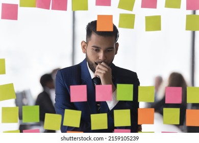 Thoughtful Indian businessman review notes written information on post-it stickers looks concentrated and concerned, deep in thoughts, search business ideas or solutions, makes tasks analysis concept - Shutterstock ID 2159105239