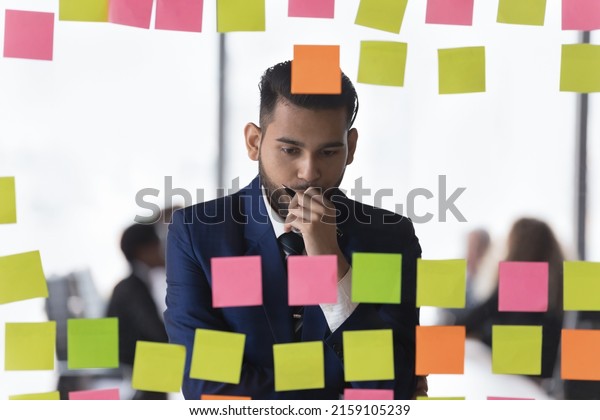 Thoughtful Indian businessman review notes\
written information on post-it stickers looks concentrated and\
concerned, deep in thoughts, search business ideas or solutions,\
makes tasks analysis\
concept