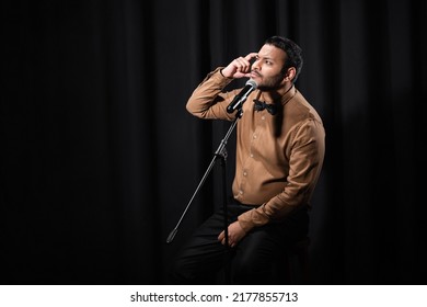 Thoughtful Indian Comedian Performing Stand Up Comedy And Telling Jokes In Microphone On Black