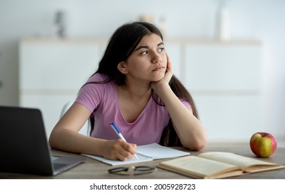 Thoughtful Indian teen girl studying online from home, taking notes during web lesson, feeling bored at home. Pensive adolescent participating in dull lecture, learning remotely during covid lockdown - Shutterstock ID 2005928723