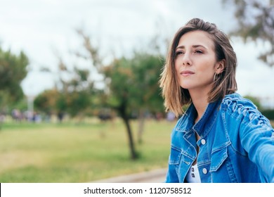 Thoughtful introvert young woman sitting outdoors in a park looking into the distance with a contemplative serious expression with copy space