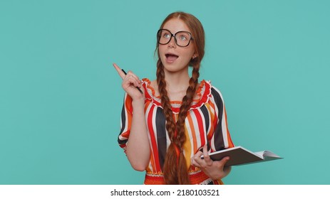 Thoughtful Journalist Redhead Girl Making Notes, Writing Down Thoughts With Pen Into Notepad Notebook Diary, To Do List, Good Idea. Young Teenager Ginger Child Kid Isolated On Blue Studio Background