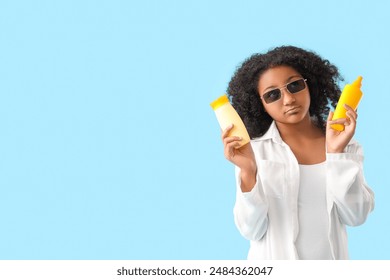 Thoughtful little African-American girl with bottles of sunscreen cream on blue background - Powered by Shutterstock