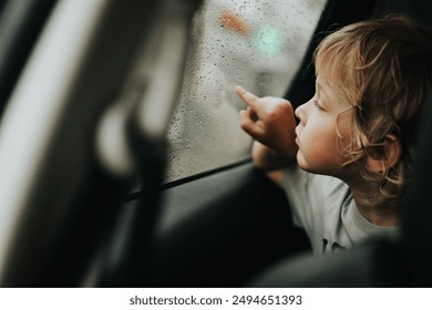 Thoughtful little blond baby boy seated in car backseat looking through rain covered window in rainy day. - Powered by Shutterstock