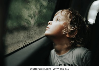 Thoughtful little blond baby boy seated in car backseat looking through rain covered window in rainy day. - Powered by Shutterstock