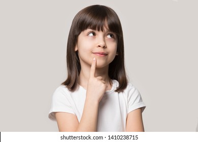 Thoughtful little girl brown-haired child touch chin with finger thinking or considering, pensive lovely daughter making decision imagining idea posing isolated on beige studio background - Shutterstock ID 1410238715