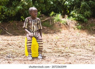Thoughtful lonely little black boy sitting on a yellow water canister by the roadside somewhere in West Africa