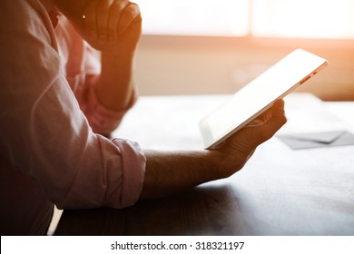 Thoughtful Male Person Looking To The Digital Tablet Screen While Sitting In Modern Loft Interior At The Table, Experienced Entrepreneur Reading Some Text Or Electronic Book At The Office, Filter Sun