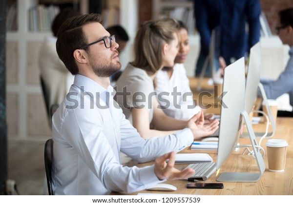 Thoughtful male worker sit in lotus position
meditating at workplace, peaceful employee practice yoga in office,
controlling emotions and staying calm, businessman clear mind or
reach nirvana state